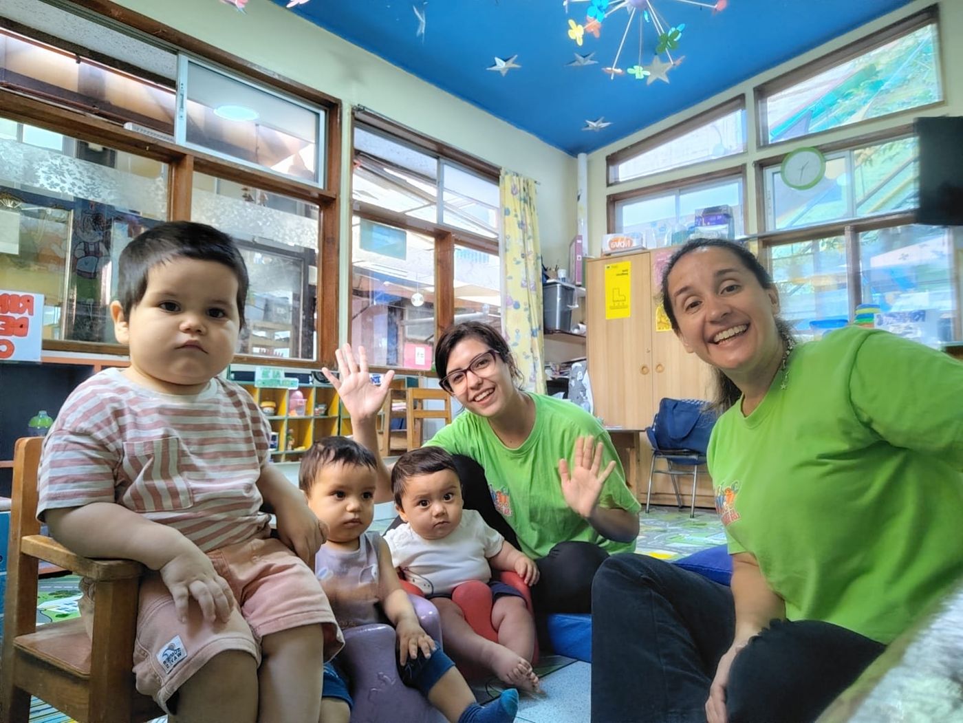 Dos educadoras del jardín sonríen sentadas junto a bebés de sala cuna en una sala luminosa