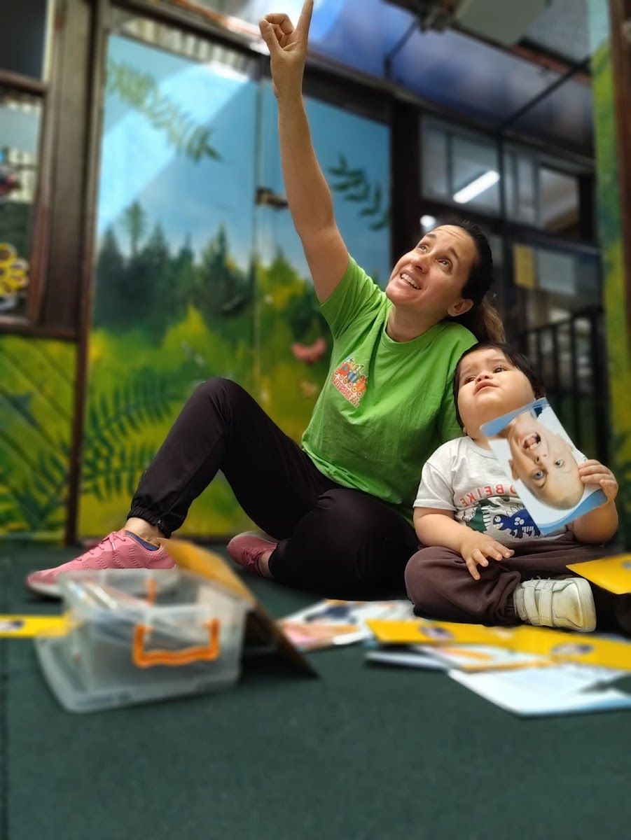 Una educadora juega sentada en el suelo con un niño pequeño en la sala de sala cuna mayor