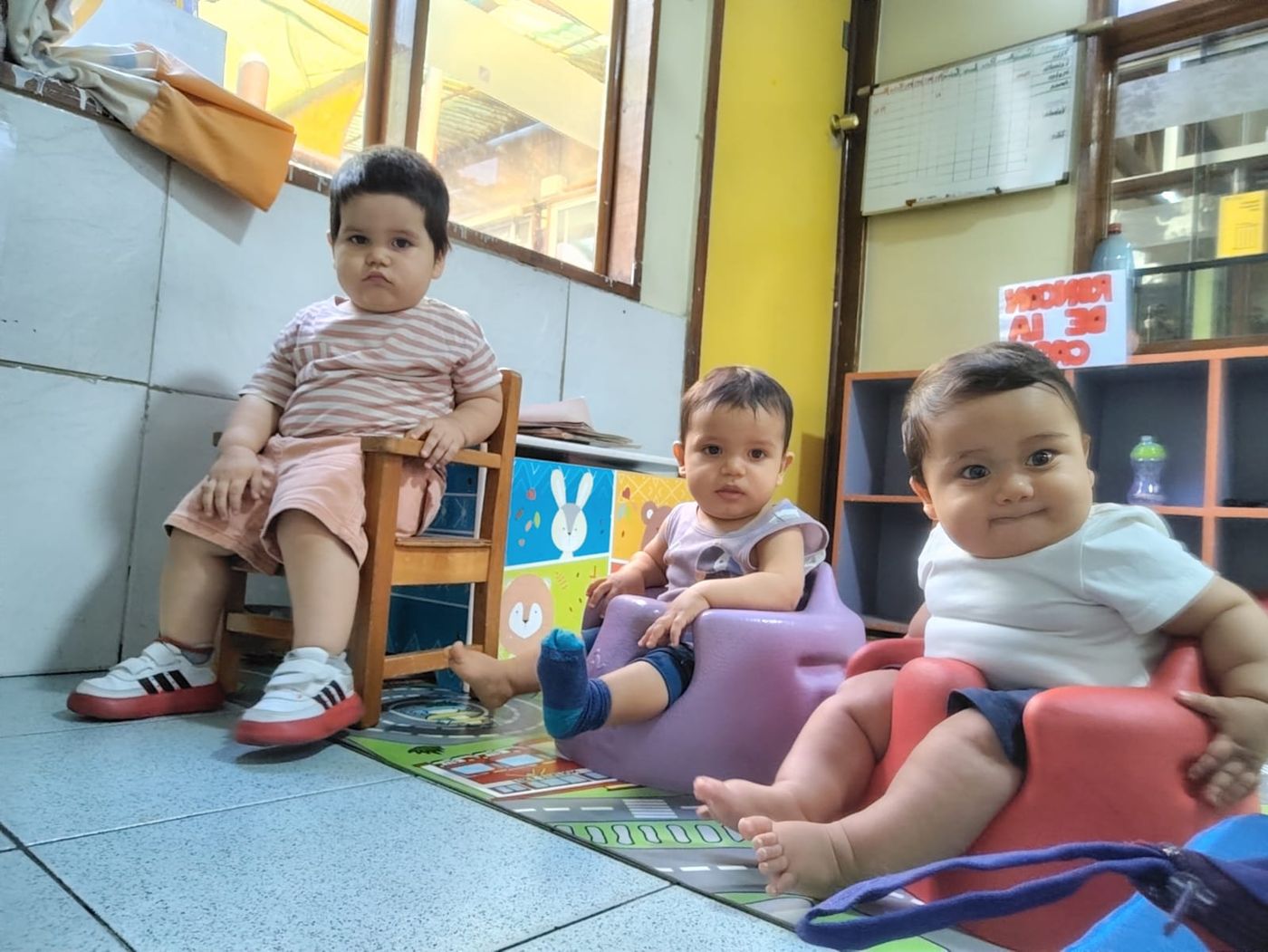 Tres bebés de sala cuna sentados en sillitas sobre una alfombra de juego