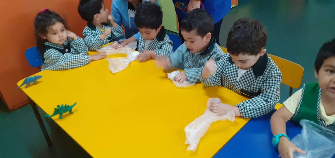 Niños con delantal cuadrillé trabajan sobre una mesa amarilla durante una actividad en sala