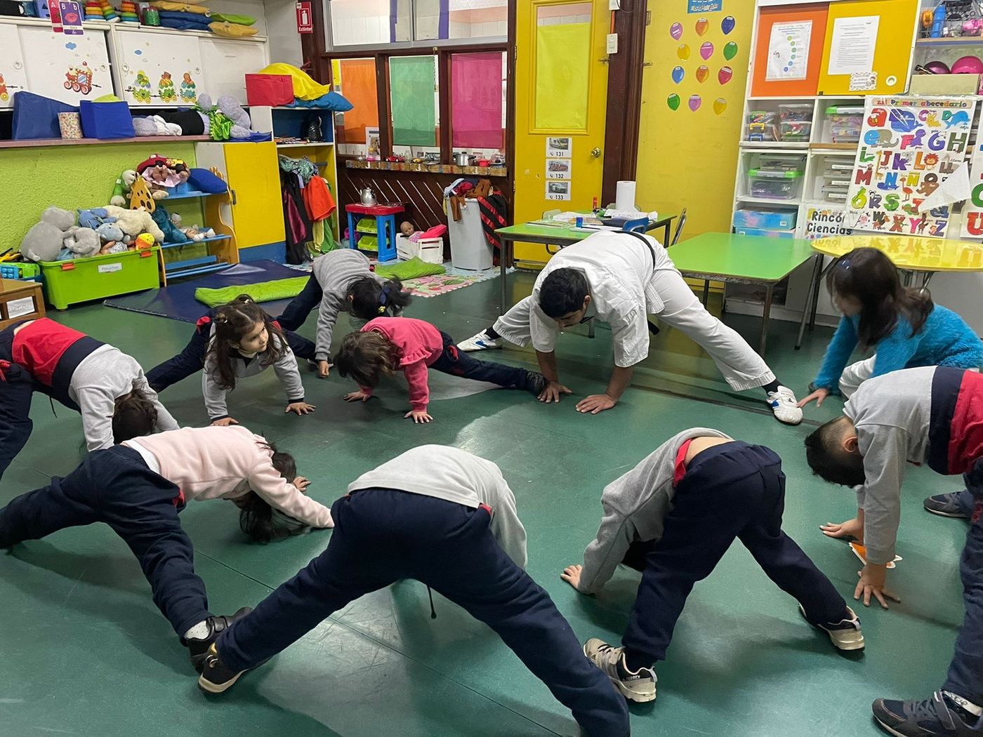 Niños y niñas del jardín practican una postura de yoga en la sala junto a su profesor